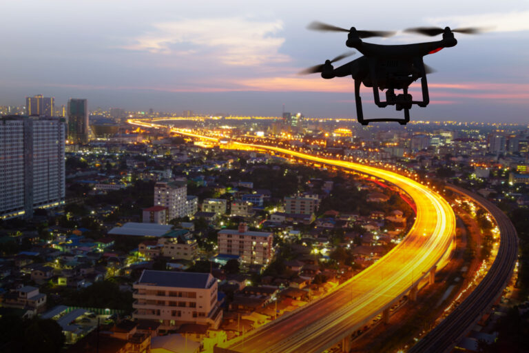 Silhouette of drone flying above city at sunset